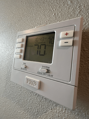 A thermostat with a digital display showing 70 degrees and buttons for fan, system, and cool off heat.